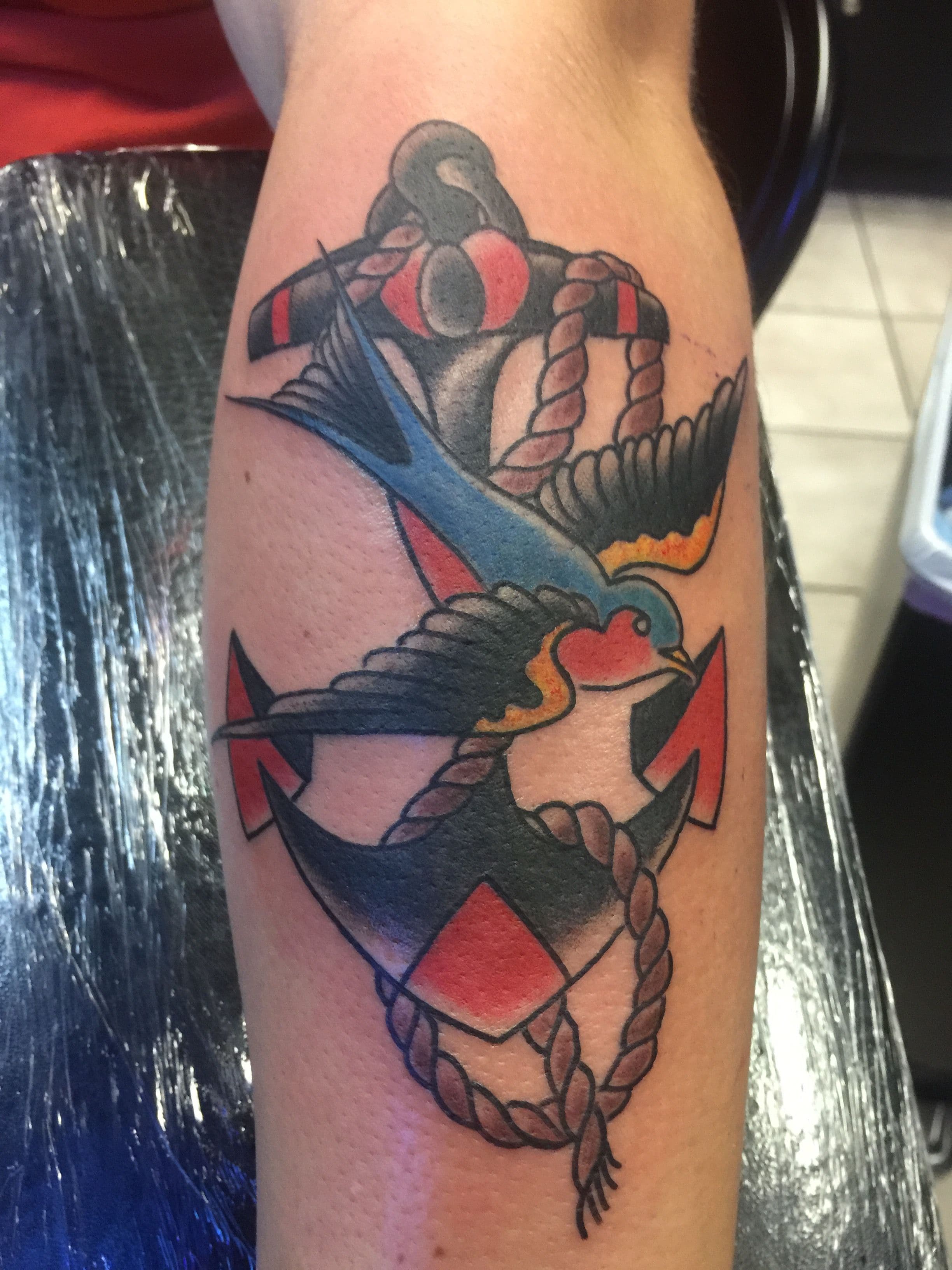 Colorful swallow and anchor tattoo on forearm in American Traditional style.