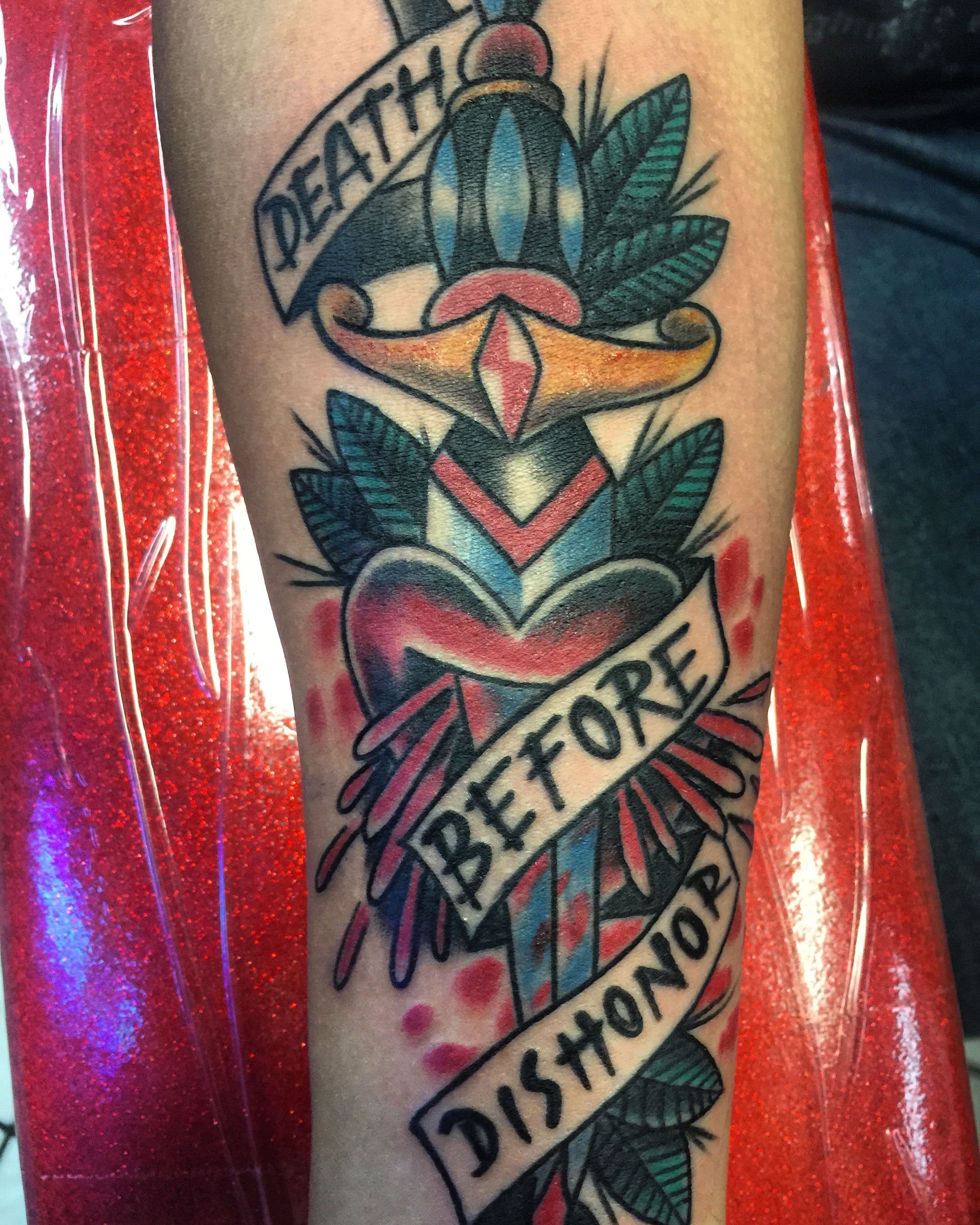 A colorful tattoo of a dagger with banners on a forearm.