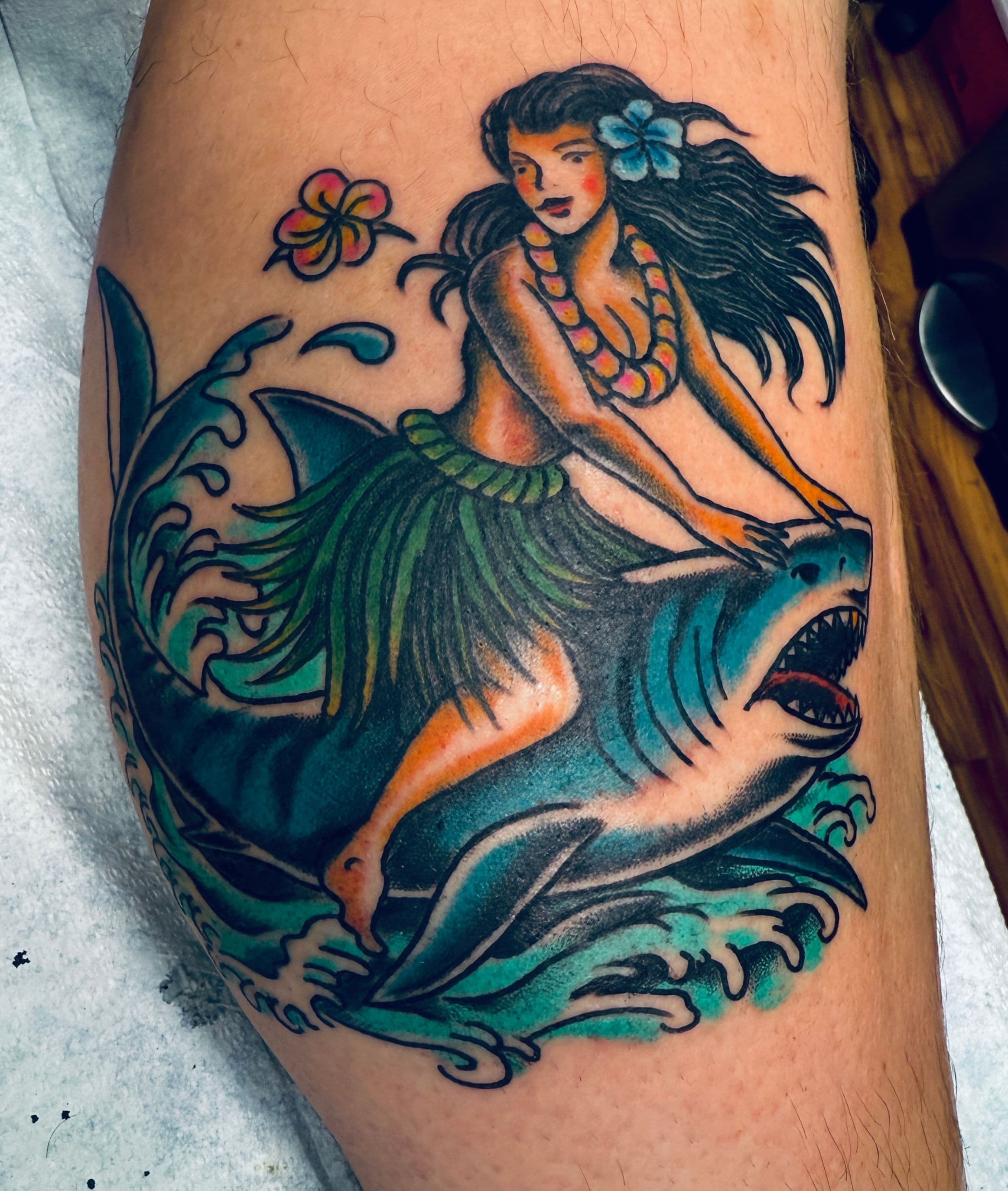 Tattoo of a hula girl riding a shark with traditional stylings.