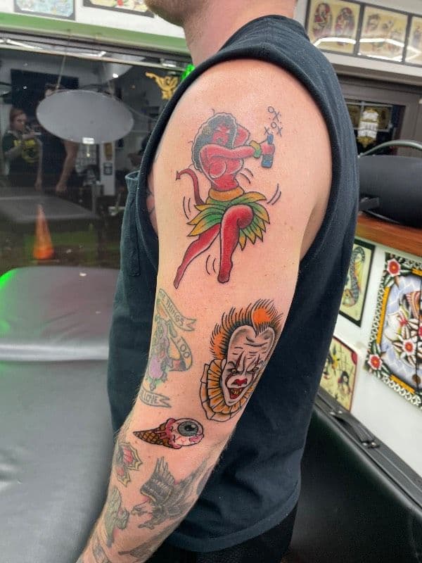 Colorful hula dancer tattoo on upper arm with other designs.