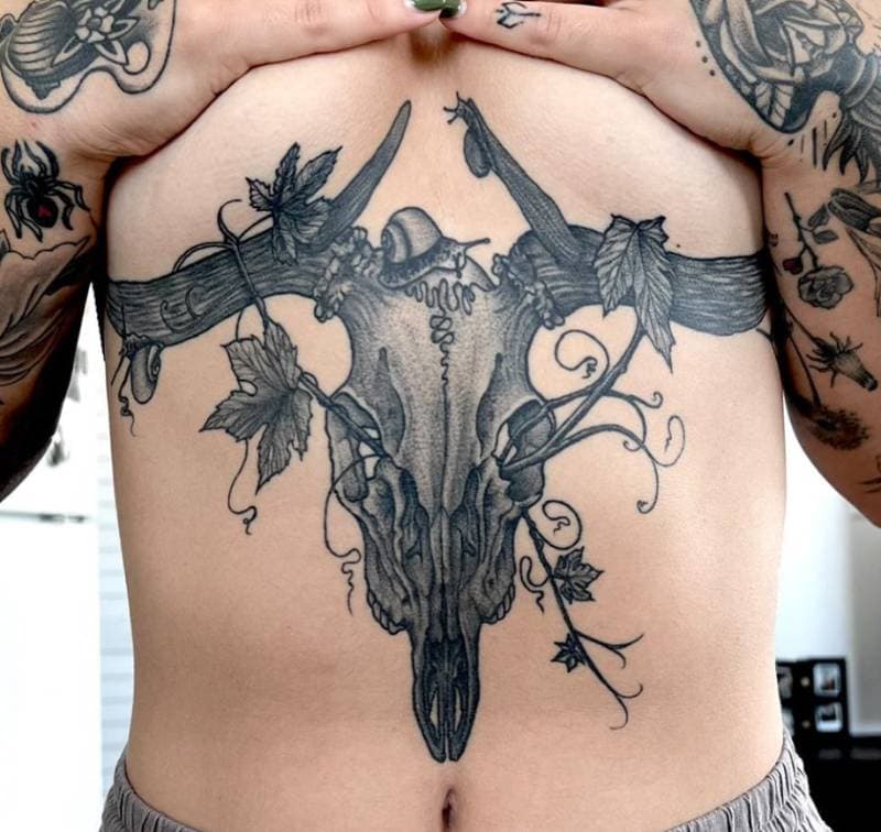Black and grey tattoo of a deer skull with ivy on a torso.