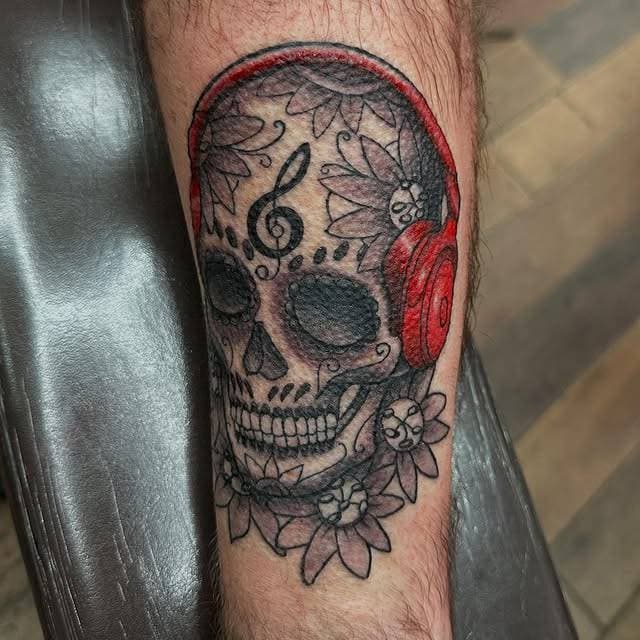 A decorative skull wearing red headphones with floral patterns tattooed on a calf.