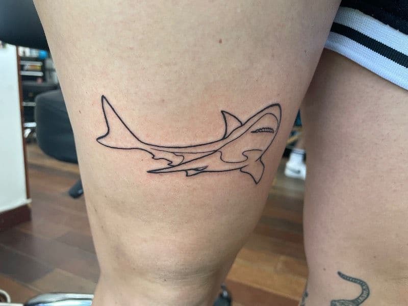 Outline of a shark tattooed on the upper thigh.